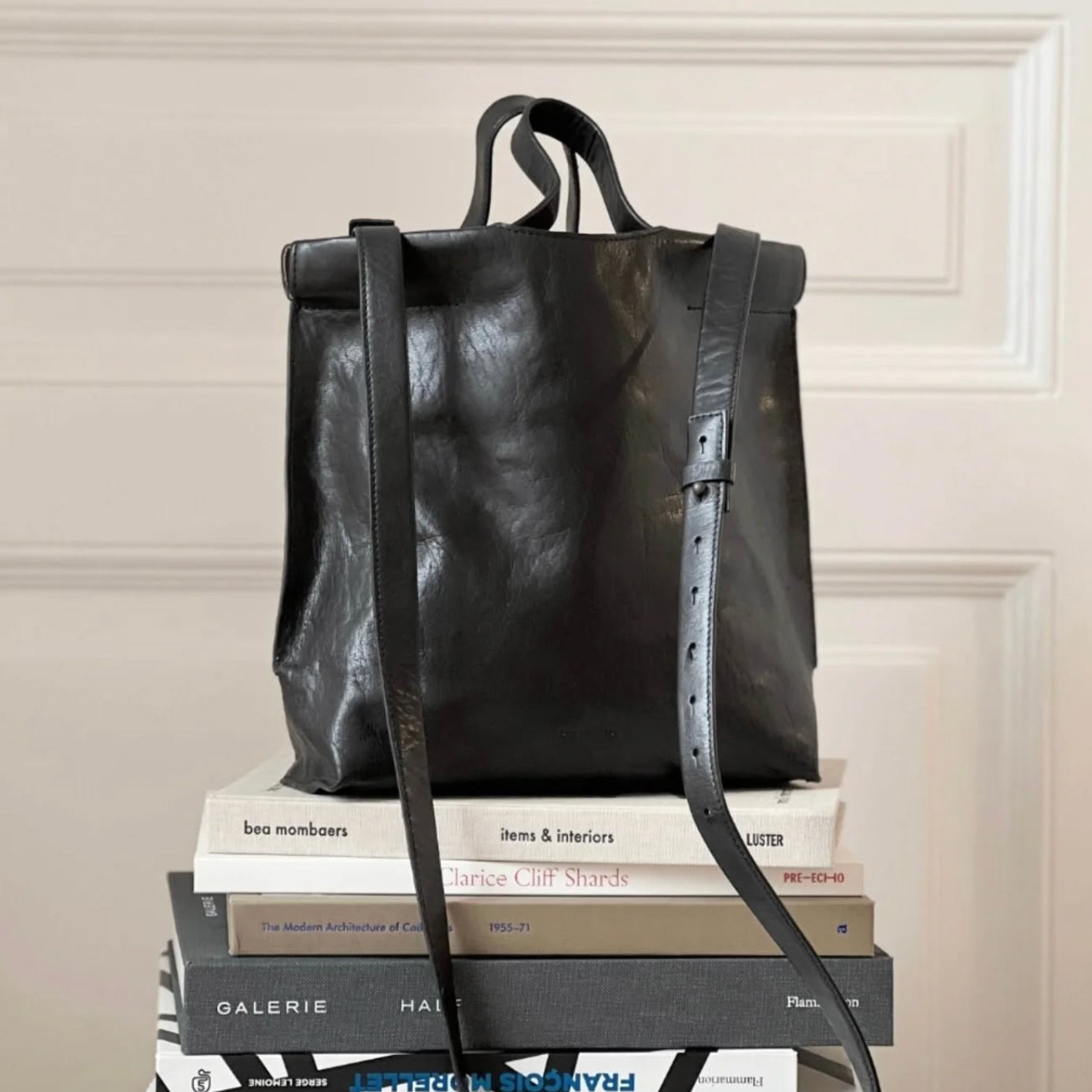 BEA MOMBAERS black leather bag displayed on pile of books