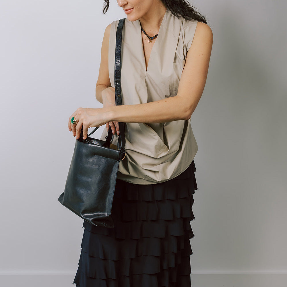 Model on grey backdrop wears tan top, black skirt and BEA MOMBAERS black leather bag