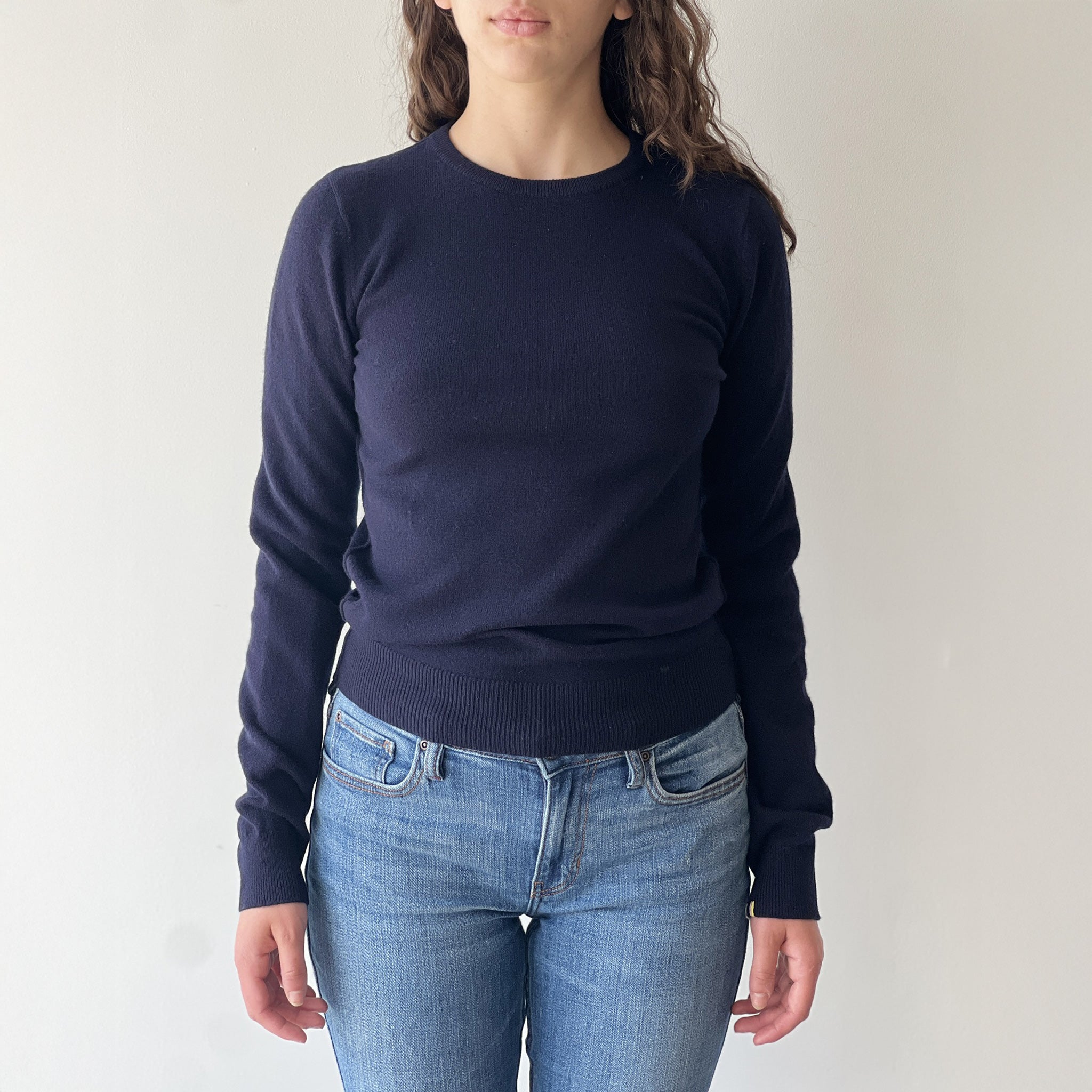 Model on grey wall wears Extreme Cashmere no. 41 Body Sweater in navy with jeans
