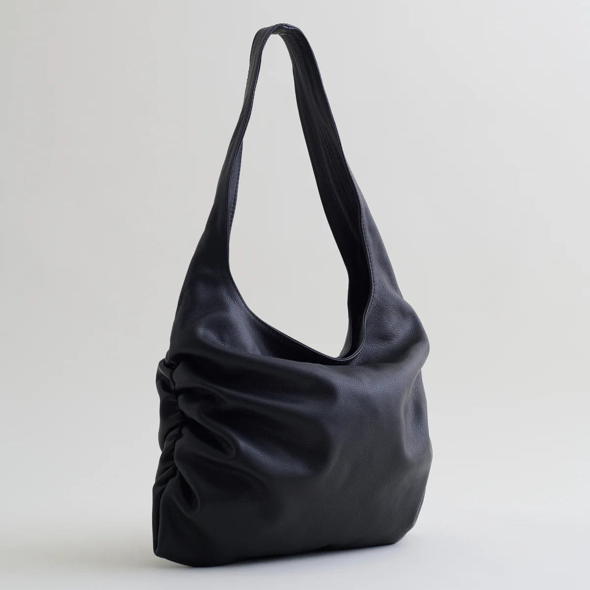 Side view of Are Studio Stella handbag in black leather on grey background.