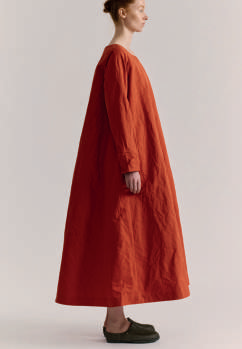 Side view of model on grey backdrop wearing Casey Casey dress in rust orange