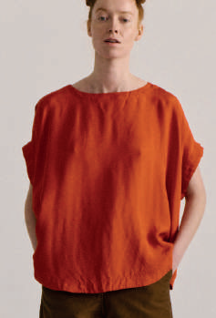 Model on grey backdrop wears Casey Casey Francesca sleeveless top in orange 