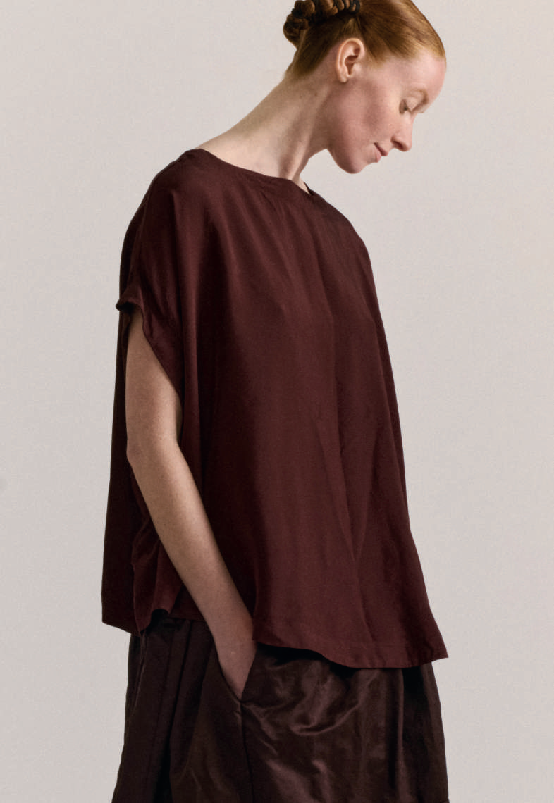 Model on grey backdrop wears Casey Casey Francesca sleeveless top in purple-brown