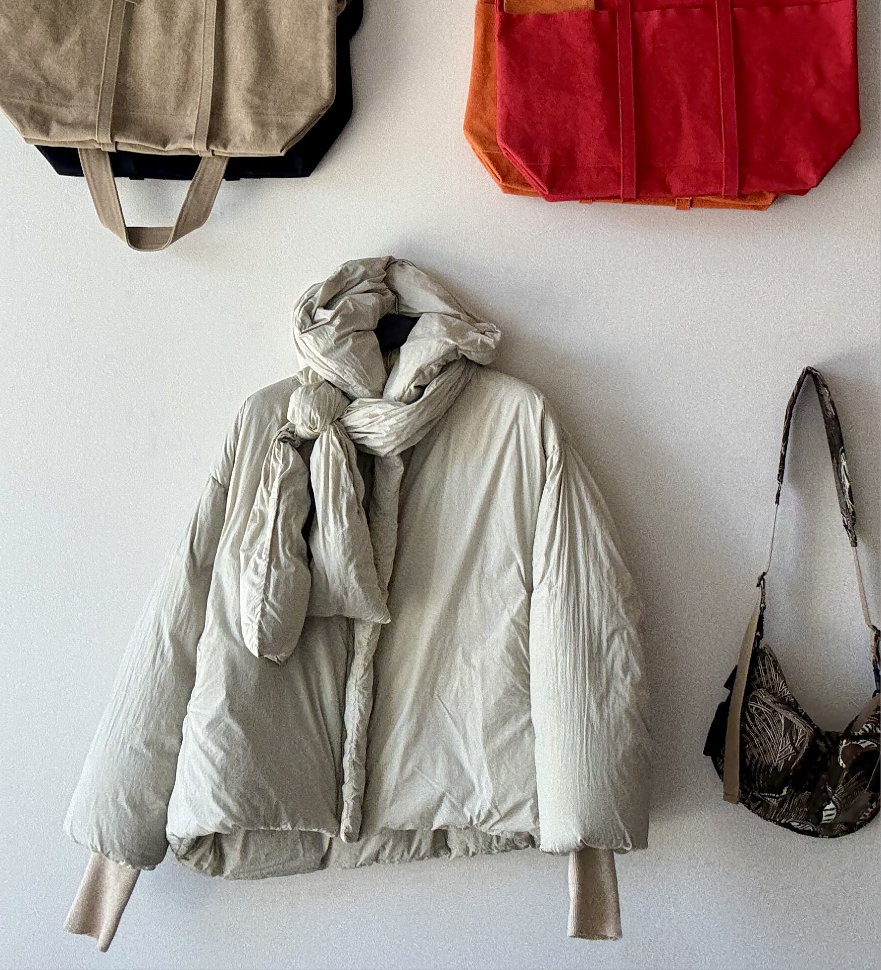 H+ HANNOH WESSEL Vaya Jacket hangs on wall with assorted bags and purses