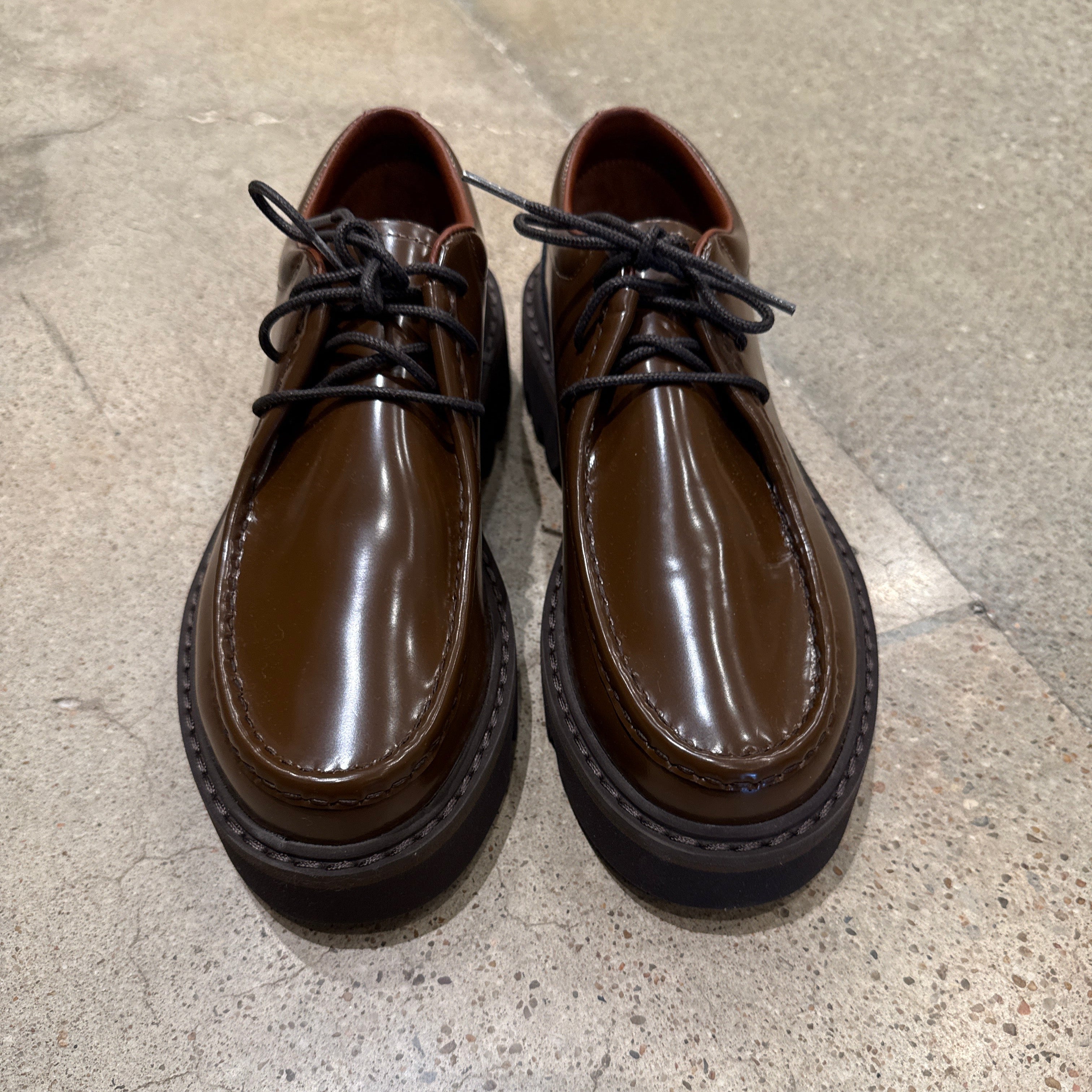 Pair of Sofie D'Hoore Falcone-LVATO shiny brown leather wallabee lace-up shoes on concrete floor.