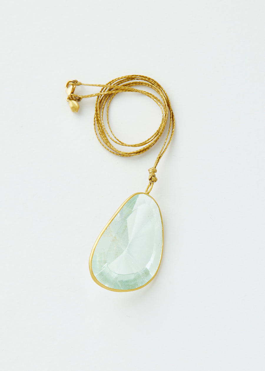 Close-up of Pippa Small Colette pendant necklace with abstract faceted aquamarine stone and rolled-up thin gold chain