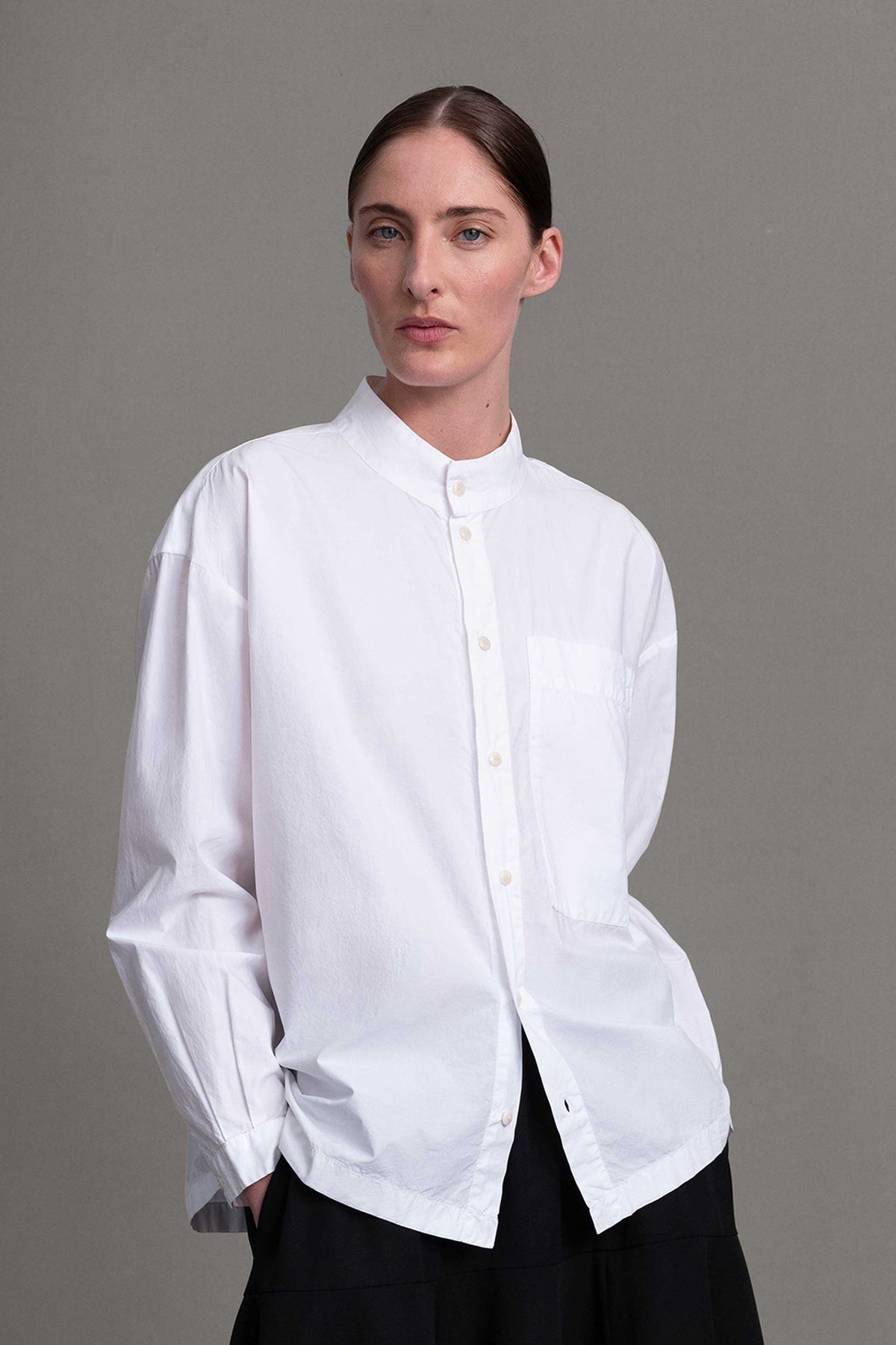 Model on grey backdrop wears alternate white Toogood The Farrier button-down Shirt