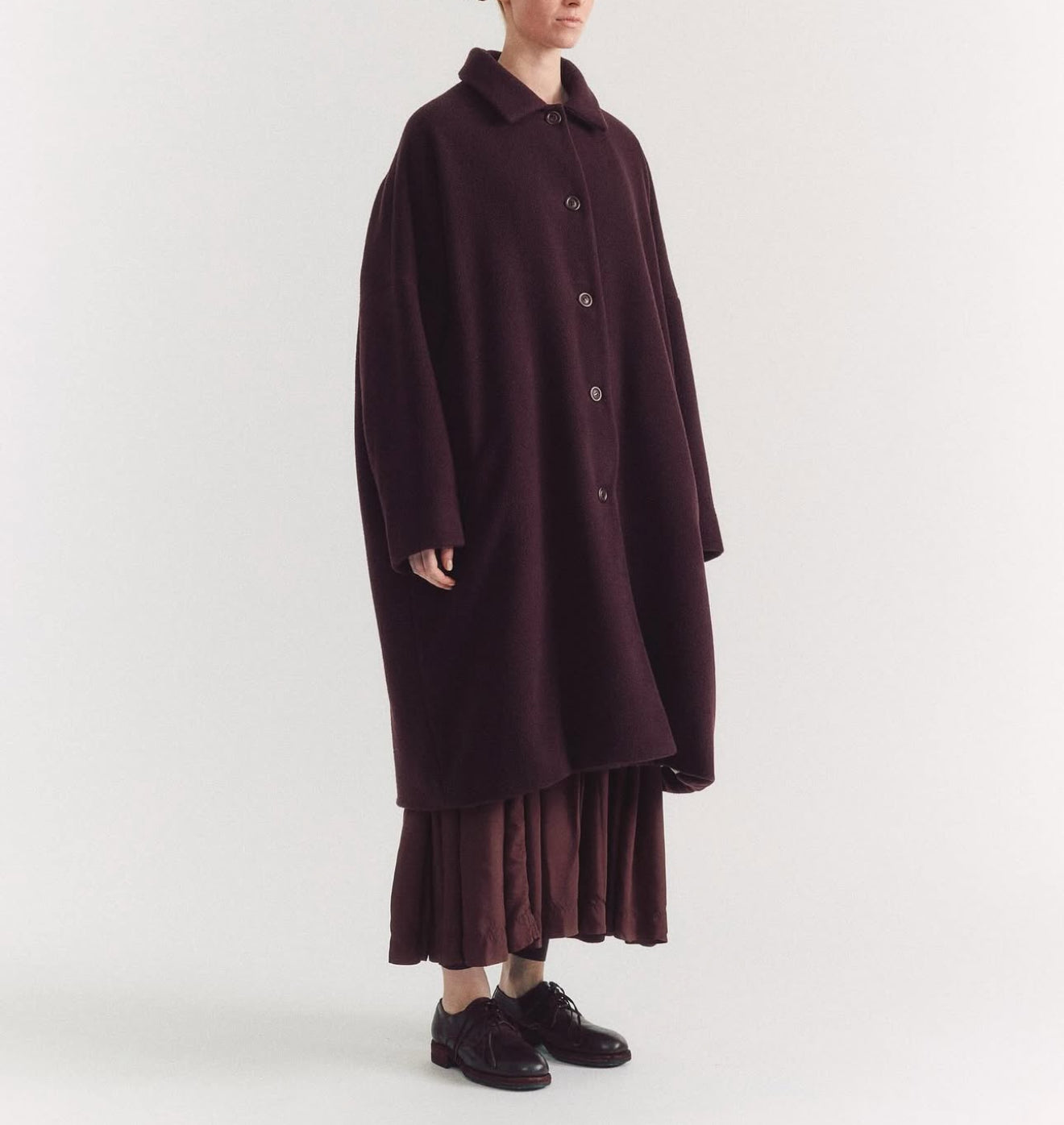Side view of model on grey backdrop wearing Casey Casey Big Blobby Coat in brown cashmere with brown skirt