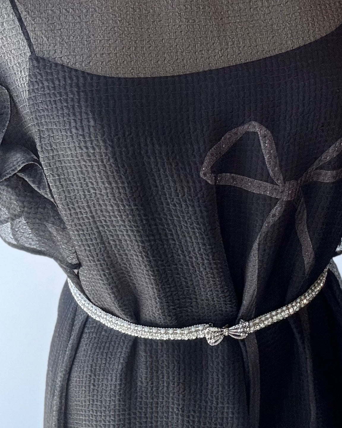 Close-up of model in black dress with Leur Logette skinny beaded bow belt at waist