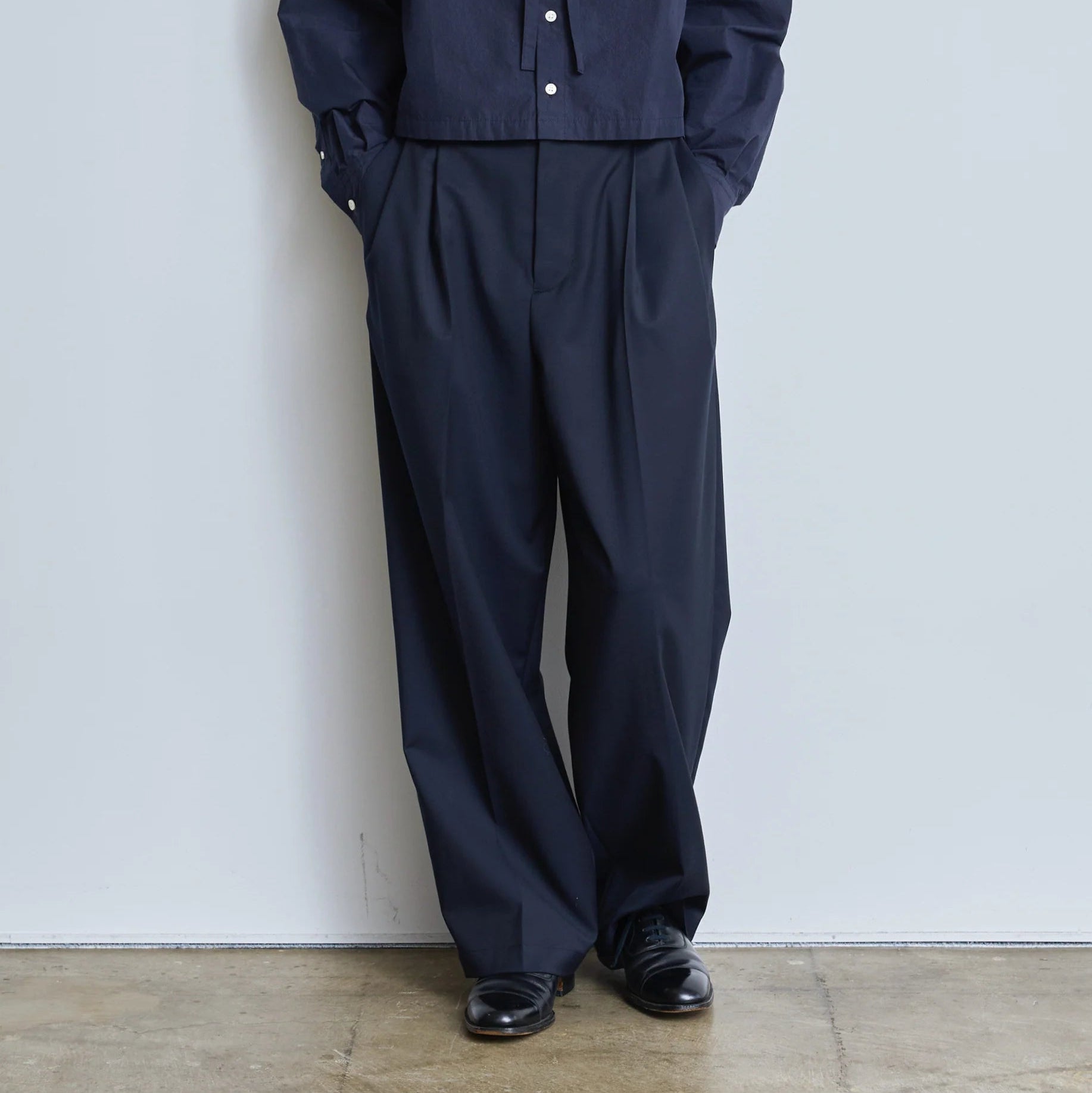 Close-up of model on grey backdrop wears Nicholson and Nicholson navy Karl-Tro Trousers with navy shirt.