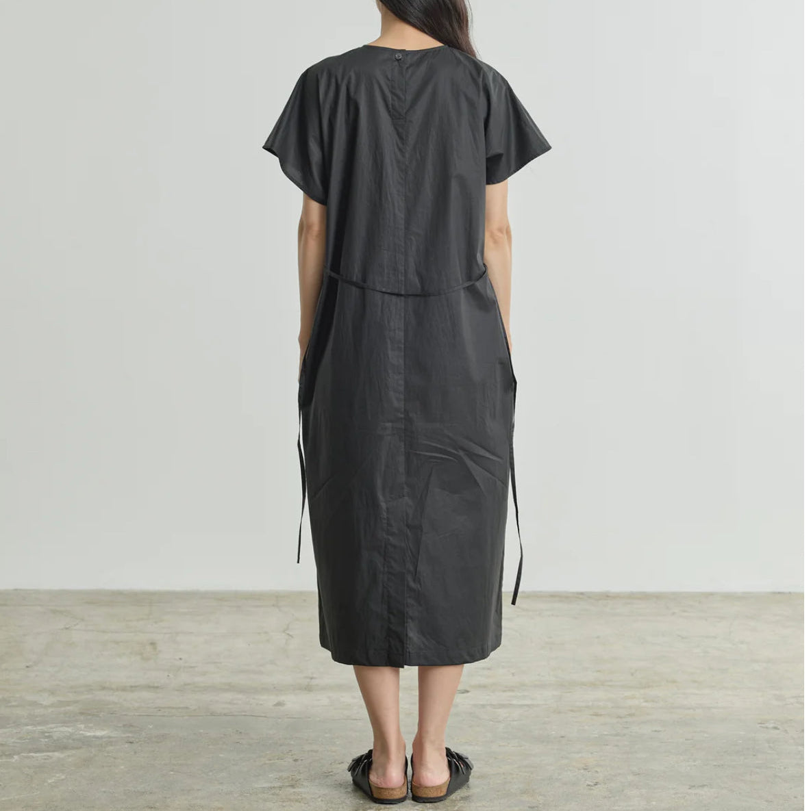 Back view of model wearing NICHOLSON & NICHOLSON loose black cotton Meg dress with black sandals