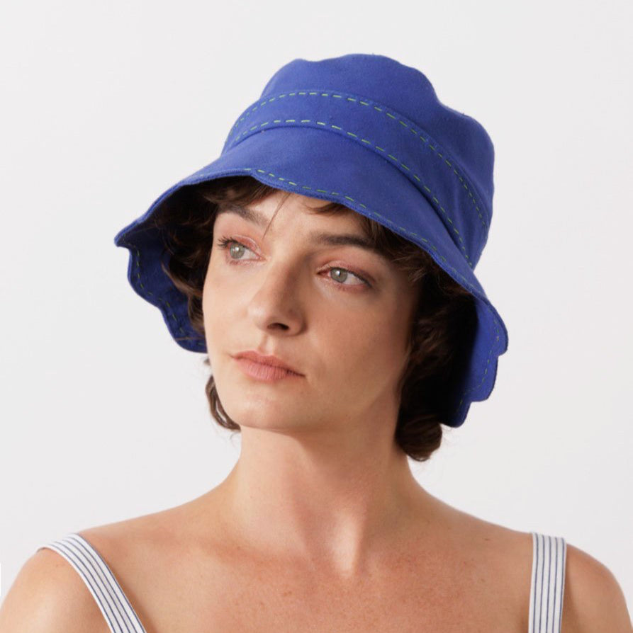 Model wears Lola Hats Coquillette Bucket Hat in blue with scalloped trim