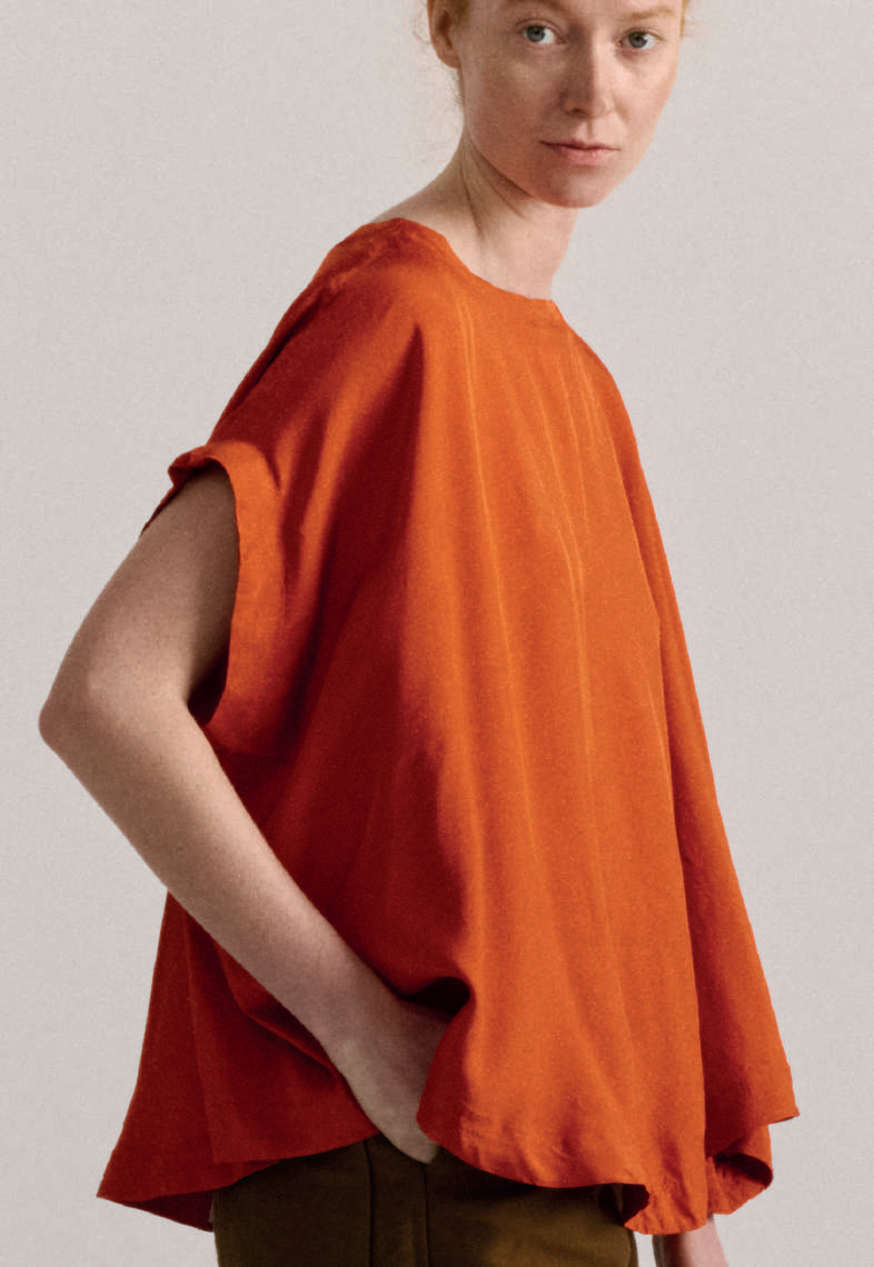 Side view of model on grey backdrop wearing voluminous Casey Casey Francesca sleeveless top in orange 