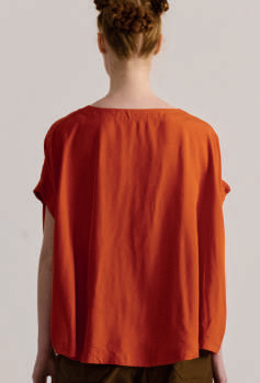 Back view of model on grey backdrop wearing Casey Casey Francesca sleeveless top in orange 