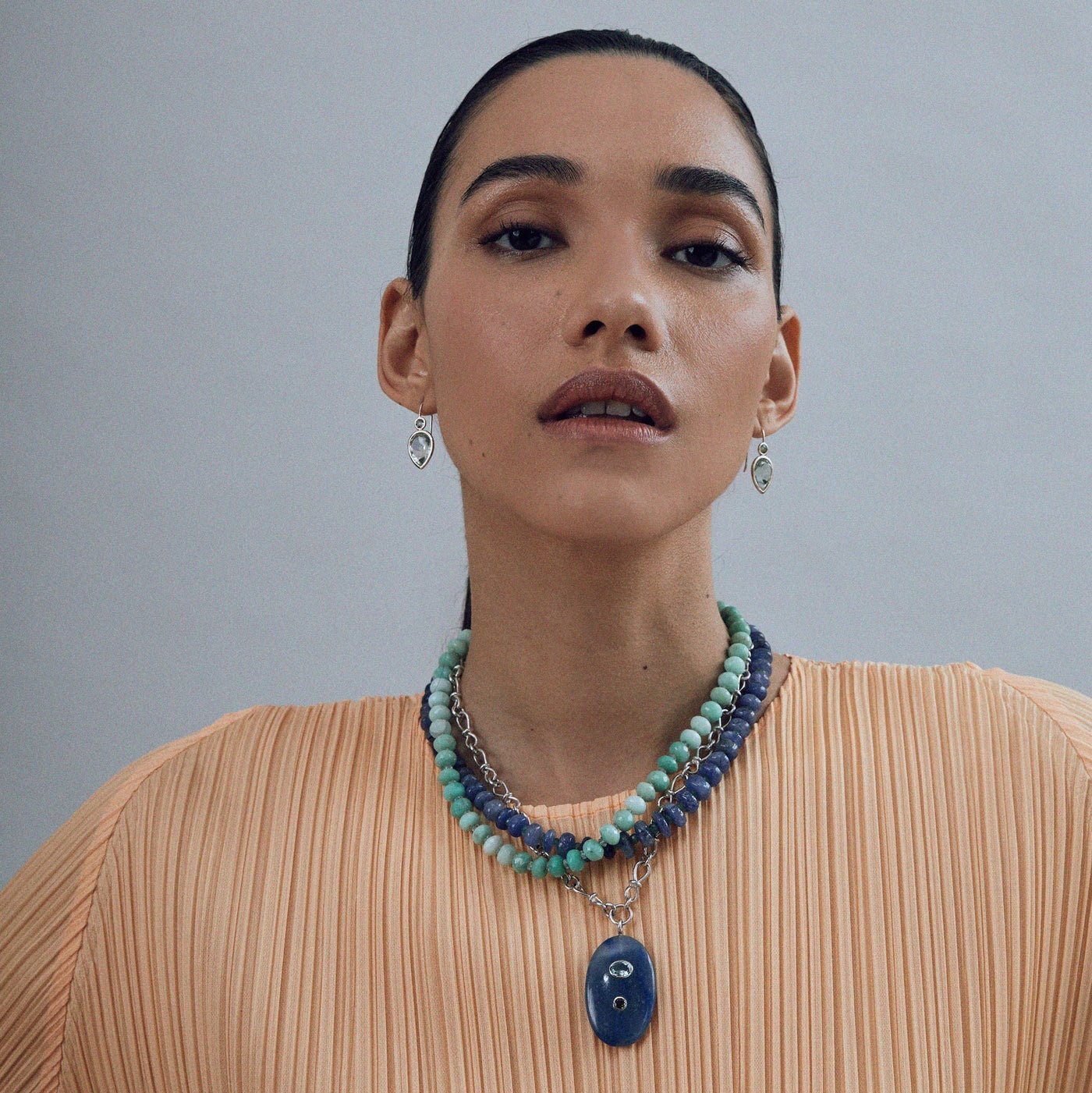 Model on grey backdrop wears Lizzie Fortunato Blue Quartz & Sterling Silver Pendant Necklace styled with bead necklaces