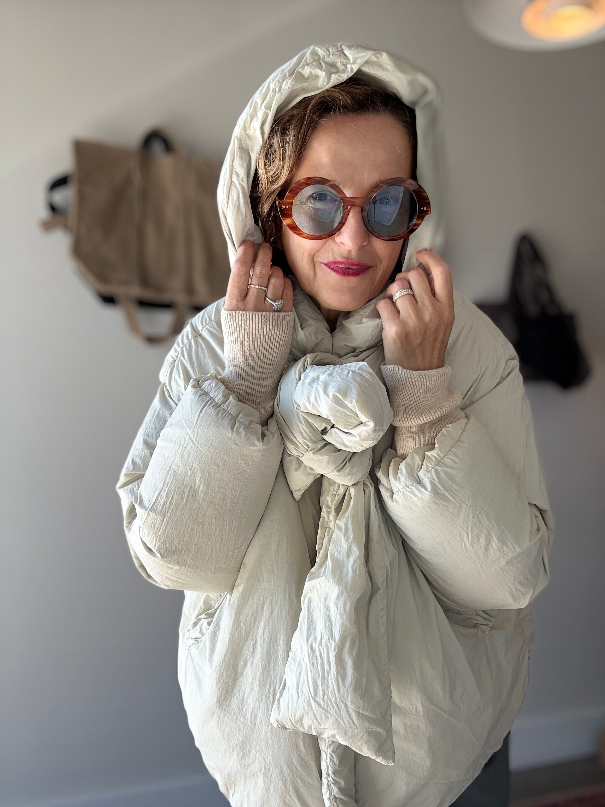 Model in studio wears H+ HANNOH WESSEL Vaya Jacket in off-white with the hood up and sunglasses 