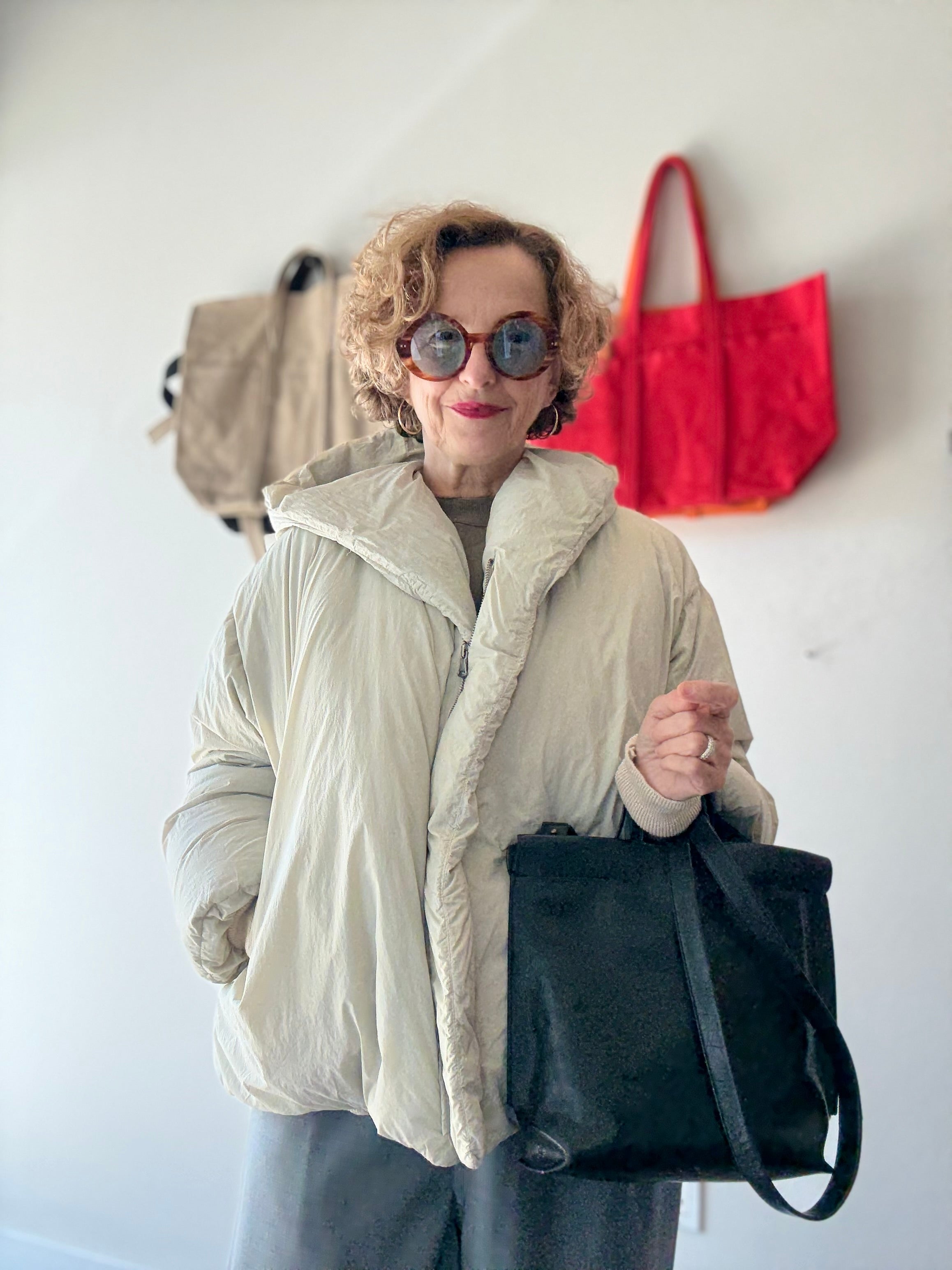 Model in studio wears H+ HANNOH WESSEL Vaya Jacket in off-white with sunglasses and black leather bag, alt view