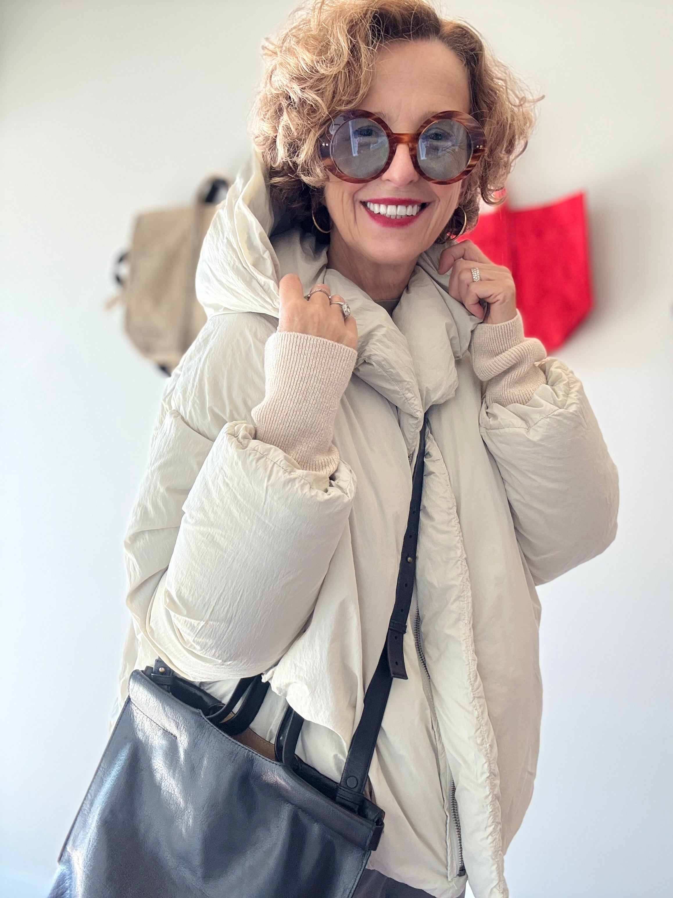 Model in studio wears H+ HANNOH WESSEL Vaya Jacket in off-white with sunglasses and black leather bag