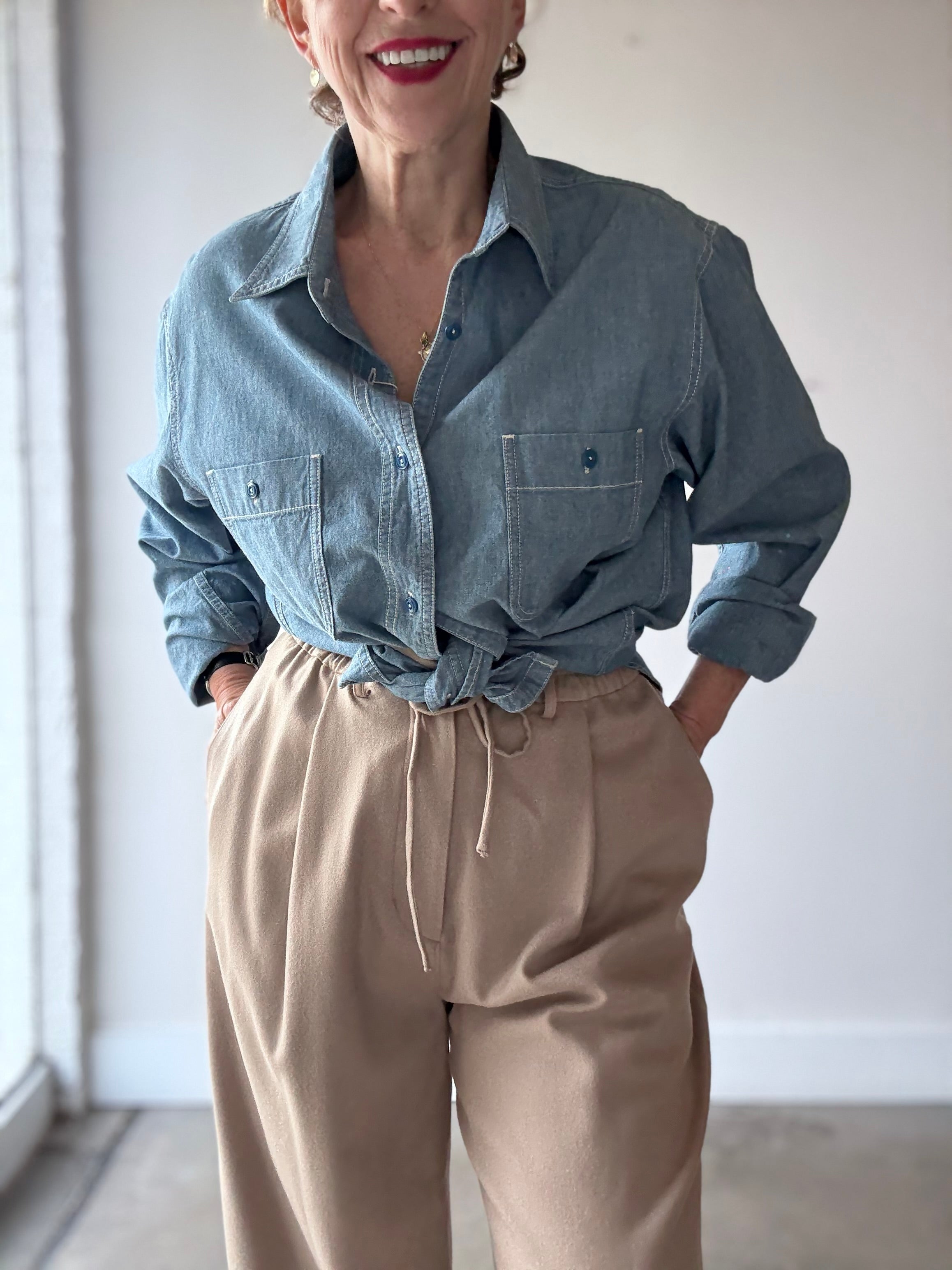 Model in studio wears CHIMALA blue chambray work shirt with sleeves rolled and tan pants