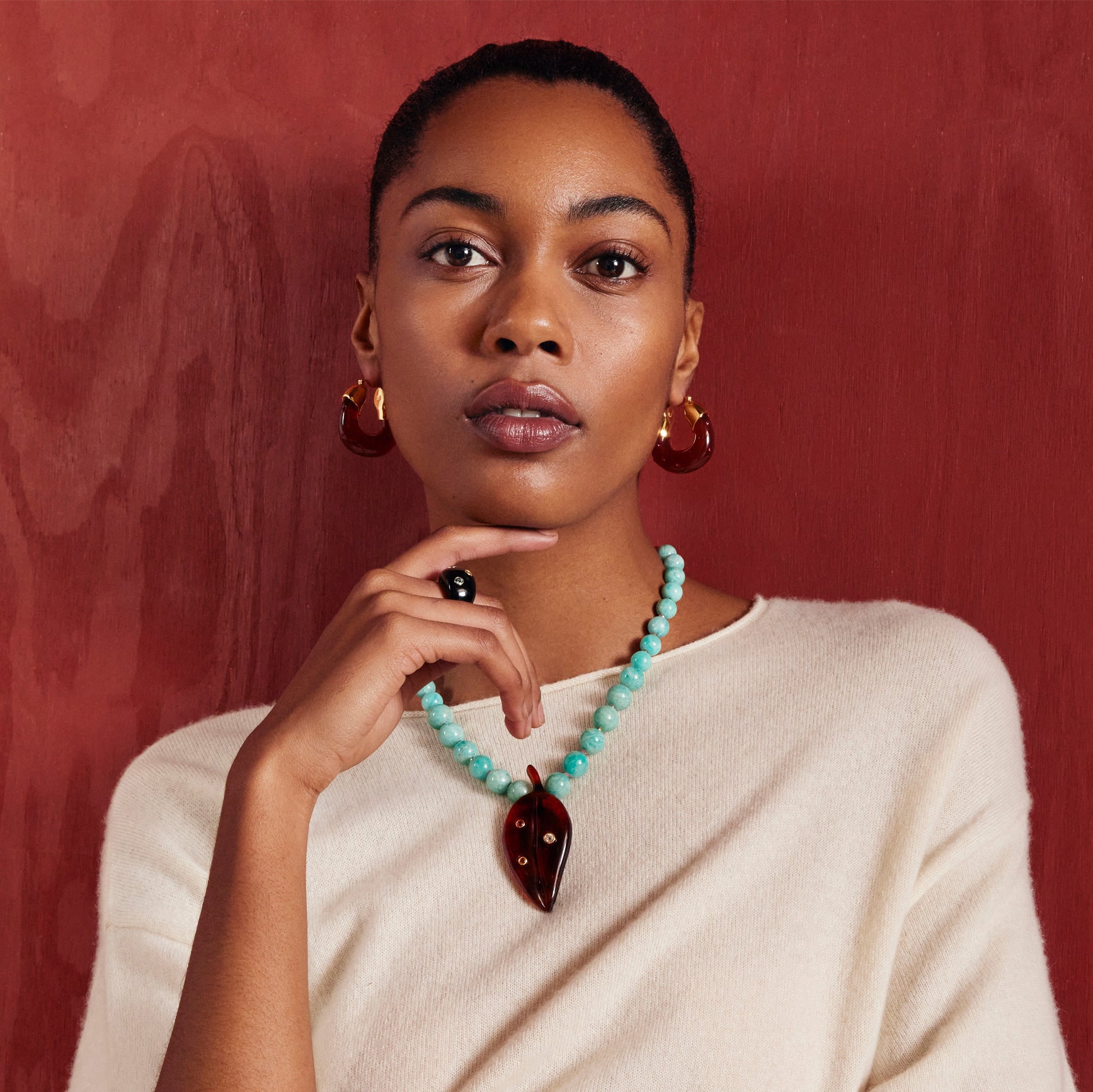 Model on burgundy backdrop wears cream knit dress with Organic Hoops in Studded Auburn