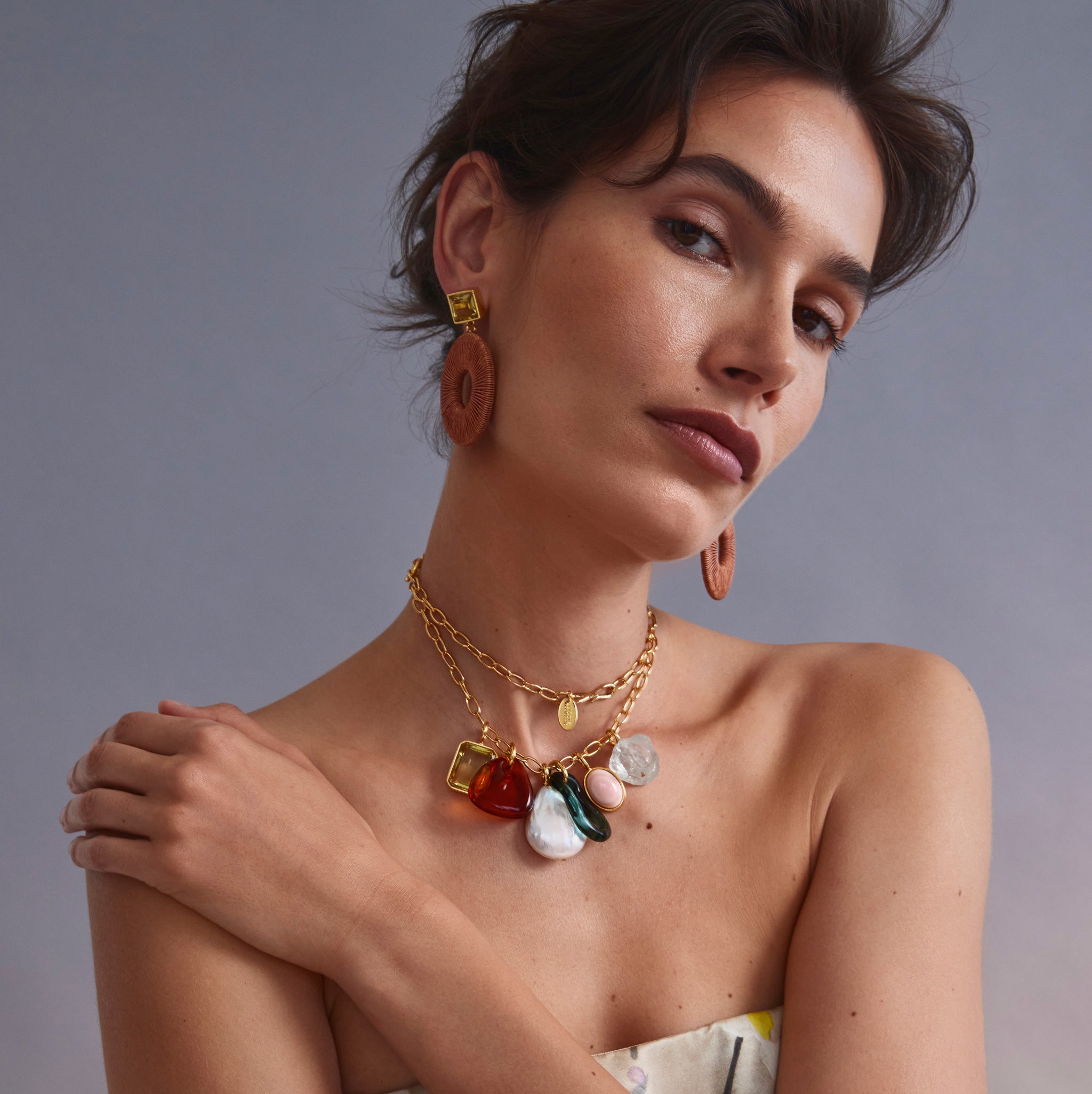 Model on grey backdrop wears strapless top with Charm Necklace and Palmier Earrings.