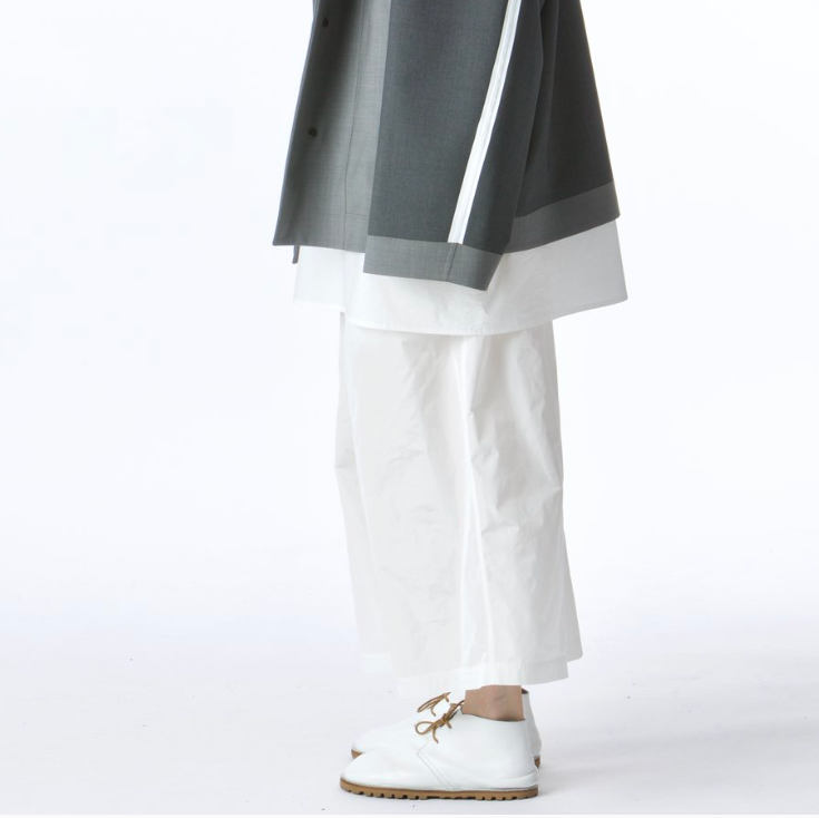 Side view of model wearing SOFIE D'HOORE Figari lace-up white leather ankle shoes with white pants and grey coat
