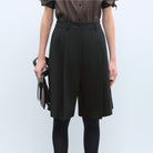 Model in close-up wears black Bermuda shorts with black stockings.