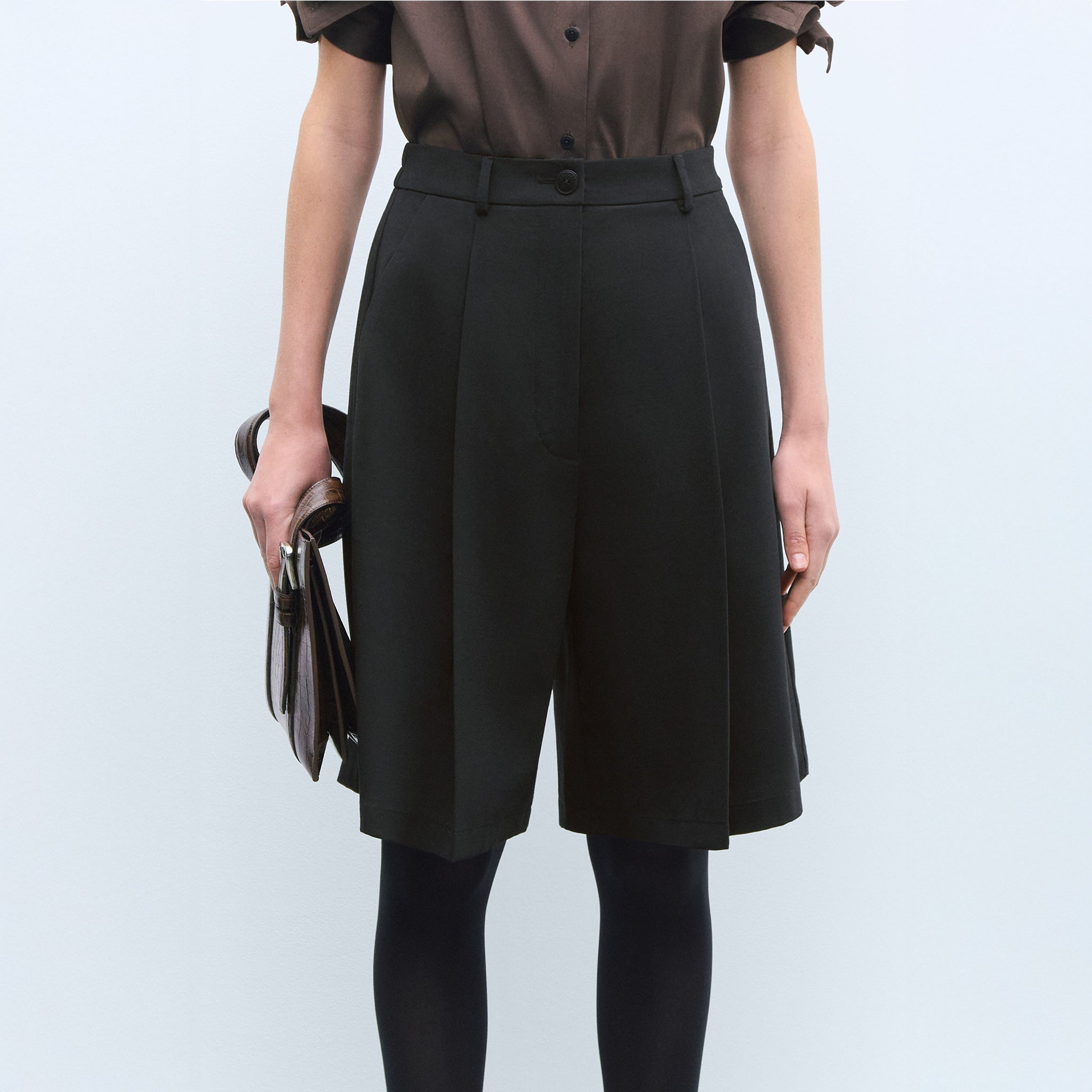 Model in close-up wears black Bermuda shorts with black stockings.